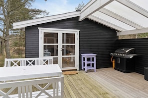 Eine Terrasse mit einem weißen Tisch und Stühlen, einem Grill und einem violetten Wagen.
