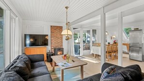 A modern living room with a sofa, a coffee table, and a TV. There is a brick fireplace and a dining area with a table and chairs. - "Poul" - 1.9km from the sea by Interhome (Blåvand)