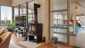 A modern interior with a wood-burning stove, a large window overlooking a pool, and a seating area with a television.