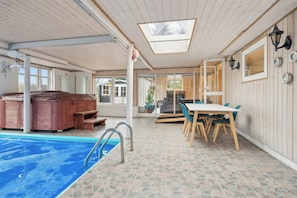 A pool area with a hot tub, a dining table with chairs, and a view of the outside.