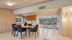 A spacious dining area with a wooden table and chairs, a kitchen in the background, and a view through a glass door.