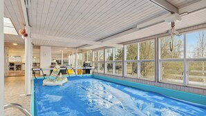 An indoor swimming pool with a blue floor, large windows, and a ceiling fan.