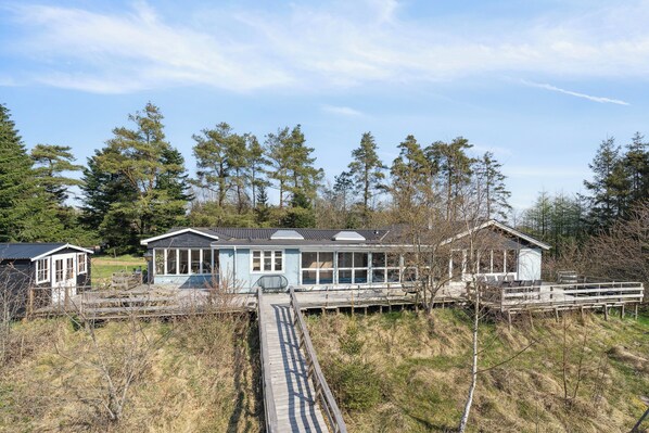 A coastal house with a wooden deck, a glass conservatory, and a small adjacent structure.