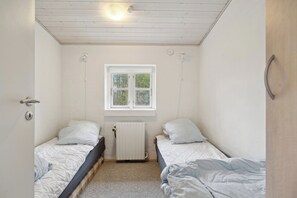 A small, single-room accommodation with two single beds, a window, a radiator, and a door.