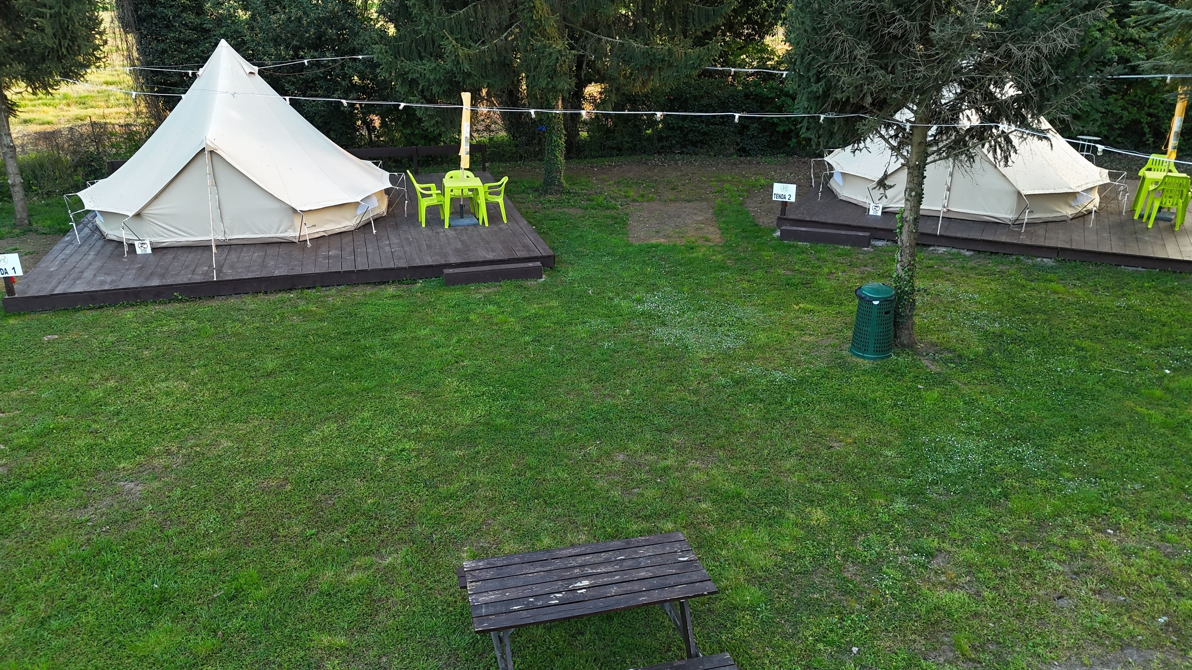 A campsite with two tents, each with a small deck and a chair. There is a picnic table in the foreground.