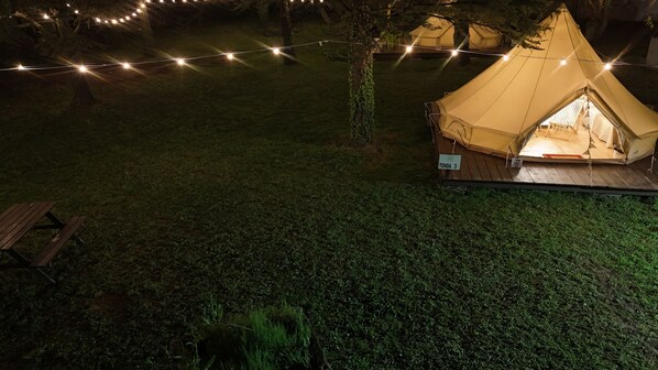 Una carpa con un letrero que dice "Tenda 3" en un área verde con luces colgantes.