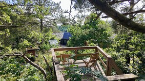 A wooden deck with chairs and a table, surrounded by trees and a house with a blue roof in the background. - VillaHou - Designer house hot tub in Hou (Hals)