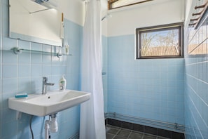 A bathroom with a white sink, a mirror, a window with a view, and blue tiled walls. - Cozy cottage near Bjerge Strand (Store Fuglede)