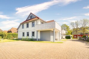 Ein zweistöckiges Haus mit Balkon und einem gepflasterten Auffahrtsweg, in dessen Nähe ein rotes Auto geparkt ist.