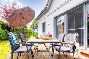 Eine Terrasse mit Tisch, Stühlen und einem Sonnenschirm, im Hintergrund ein Haus.