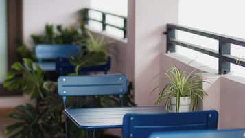 A seating area with blue metal tables and chairs, potted plants, and a balcony railing.
