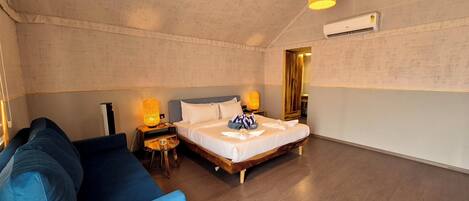 A bedroom with a bed, a blue sofa, two bedside lamps, and an air conditioning unit.