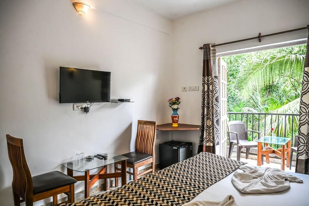 Ein Hotelzimmer mit Bett, Schreibtisch mit Stuhl, Fernseher und Balkon mit Sitzgelegenheiten.