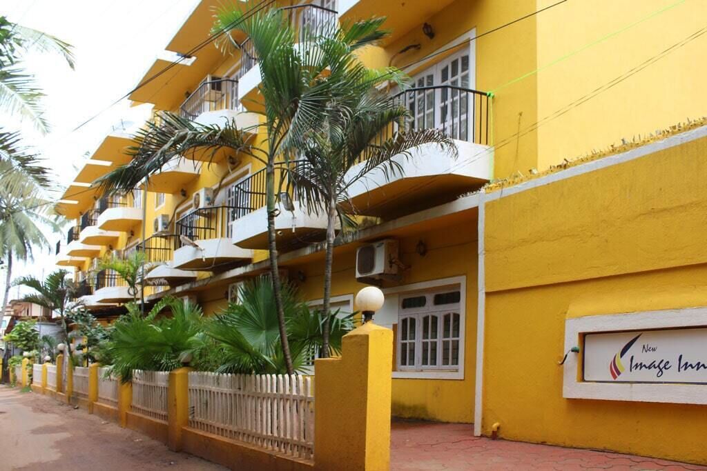 A yellow multi-story building with balconies, a sign indicating 'New Image Inn', and a fenced area with palm trees.