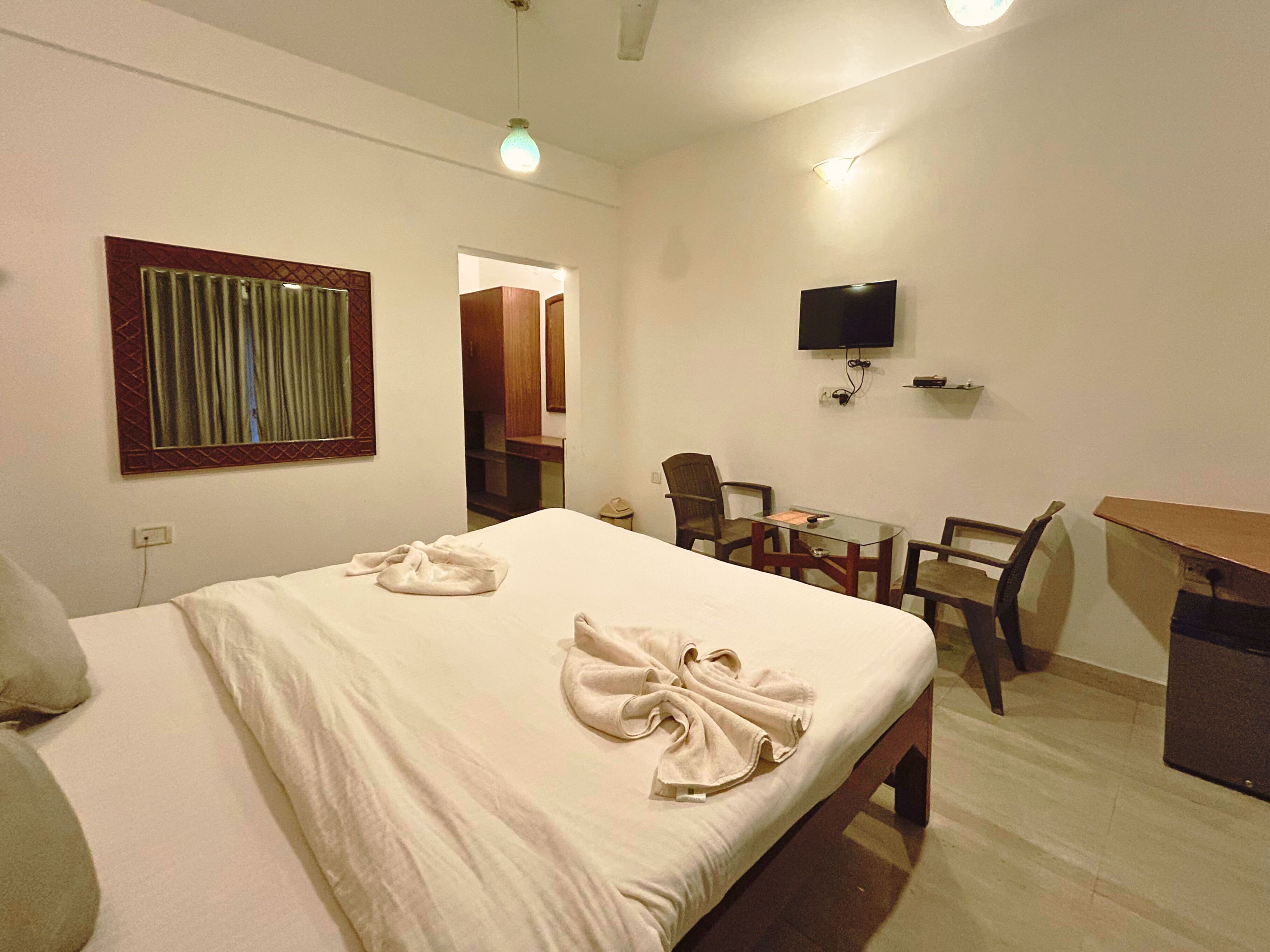 A hotel room with a bed, a desk, a chair, a television, and a mirror.