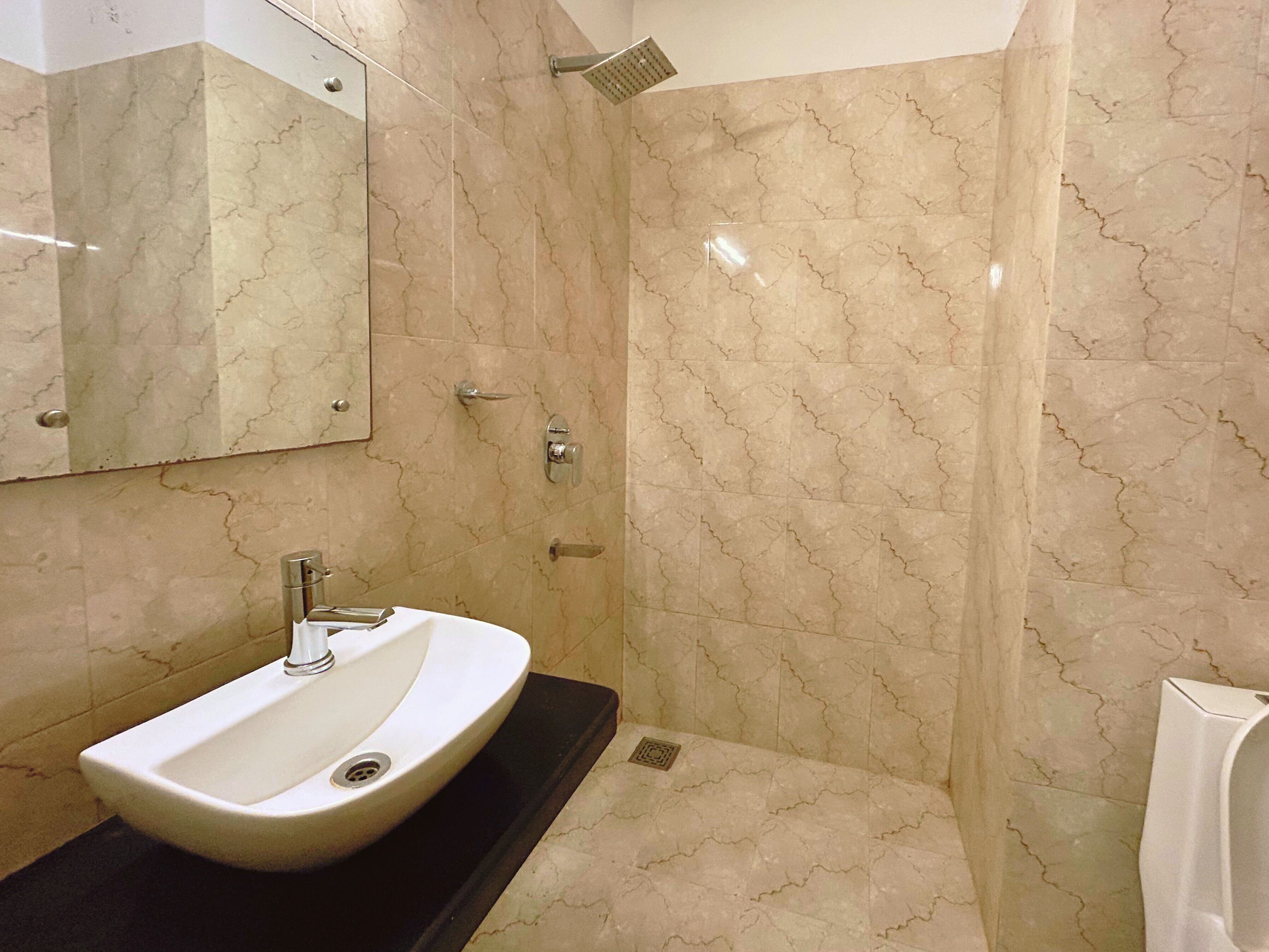 A bathroom with a sink, mirror, shower, and tiled walls.