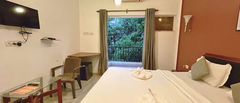 A hotel room with a bed, a desk, a chair, a TV, and a balcony with curtains.