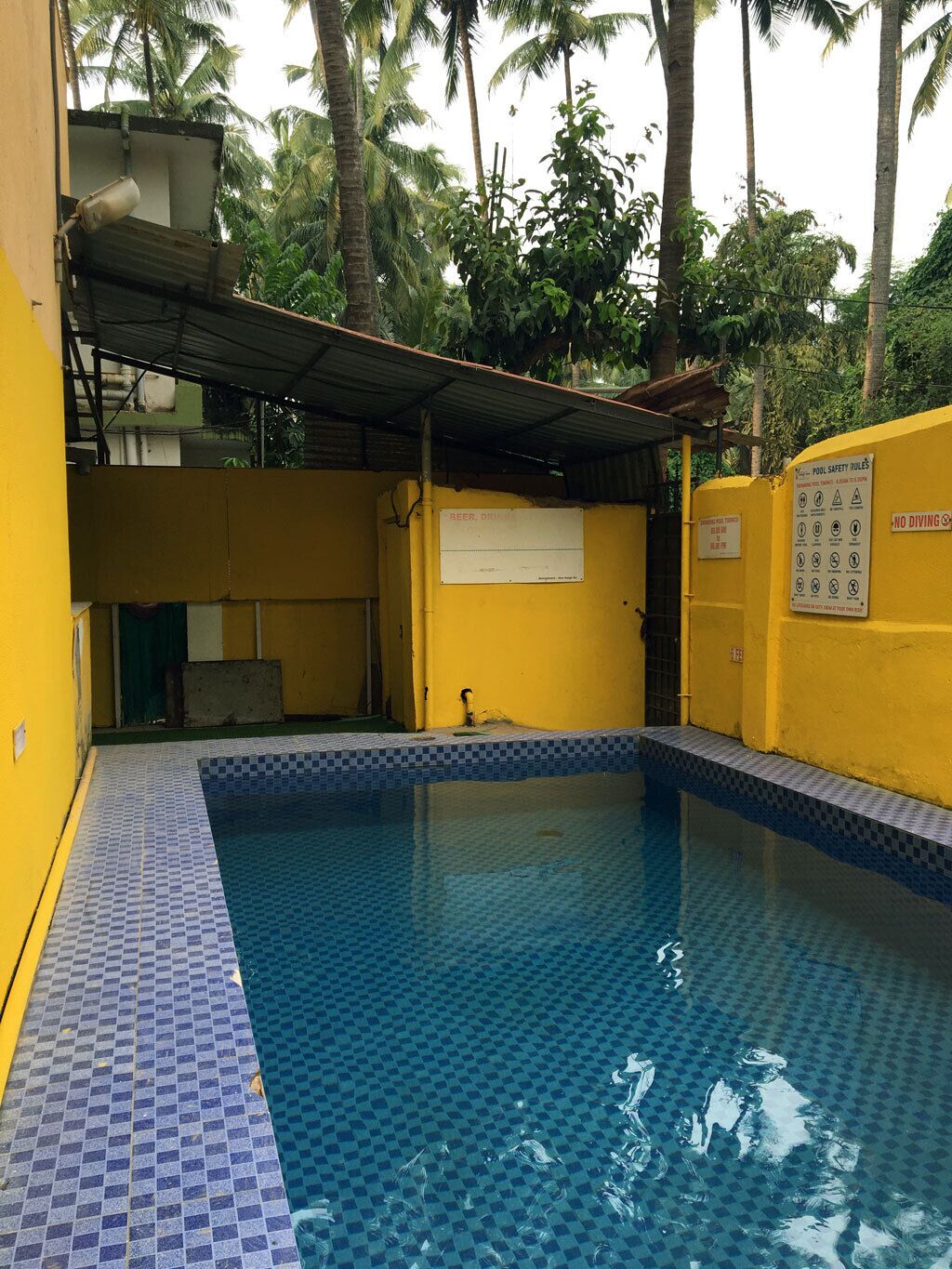 En lille swimmingpool indendørs med flisebelagt gulv og vægge, omgivet af et gult gelænder.