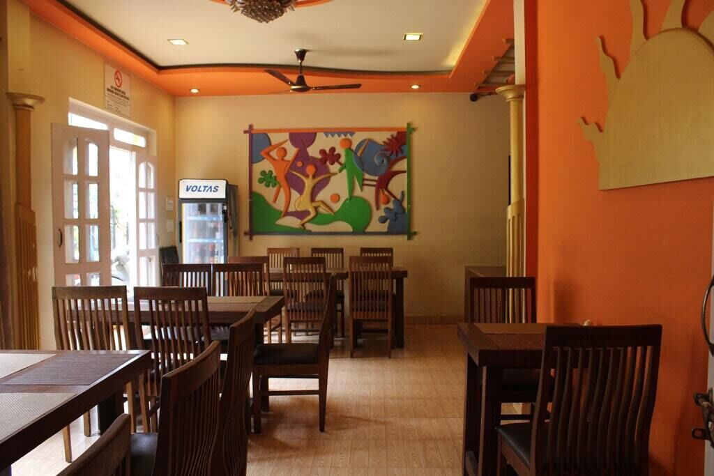 A dining area with wooden tables and chairs, a ceiling fan, and a colorful abstract painting on the wall.