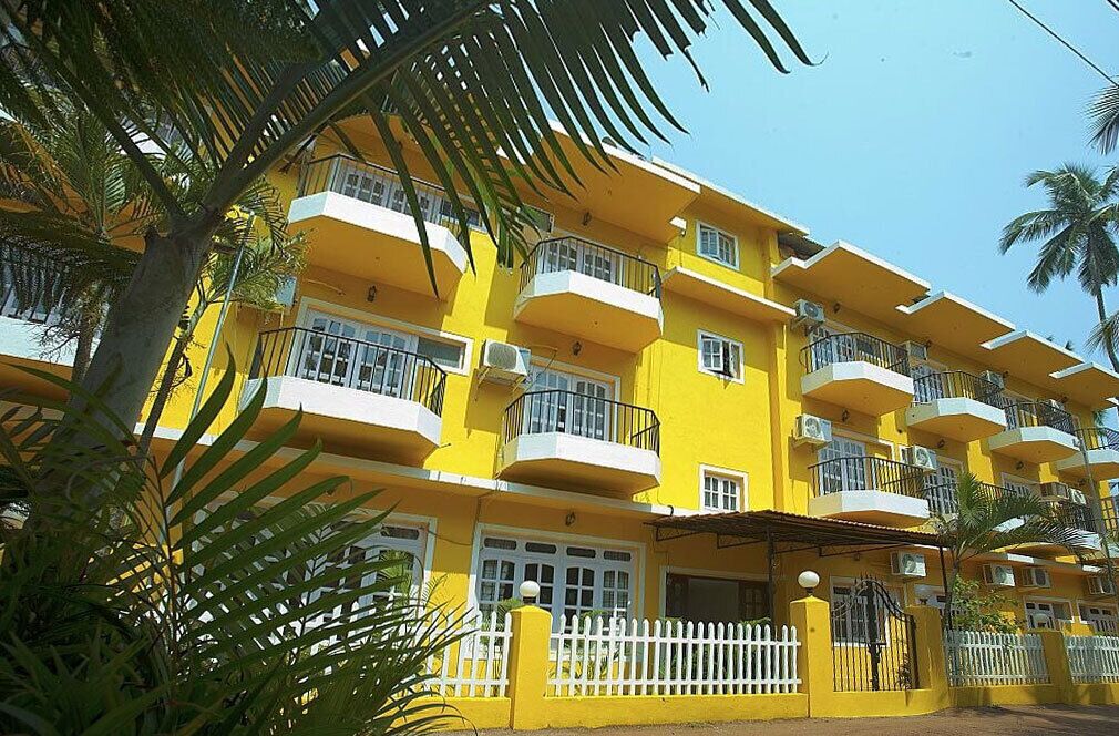 A multi-story yellow building with balconies, air conditioning units, and a white picket fence.