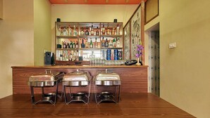 A bar area with shelves of liquor bottles, a bar counter, and three metal food containers on the counter. - Hotel Grand Image Inn (Calangute)
