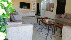 A modern living room with a flat-screen TV, beige sofas, a coffee table, and a decorative plant. - Petra Guests Home  (Wadi Musa)