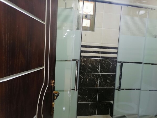 Un baño con puerta de madera, cabina de ducha de vidrio y baldosas de mármol negro.