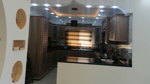 A modern kitchen with dark wooden cabinets, a black countertop, and recessed ceiling lighting. - Petra Guests Home  (Wadi Musa)