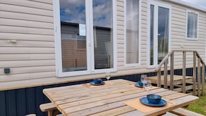 A wooden deck with a table set for dining, a glass of water, and a blue bowl. - Chalet in Belgium with Garden Terrace (Blankenberge)