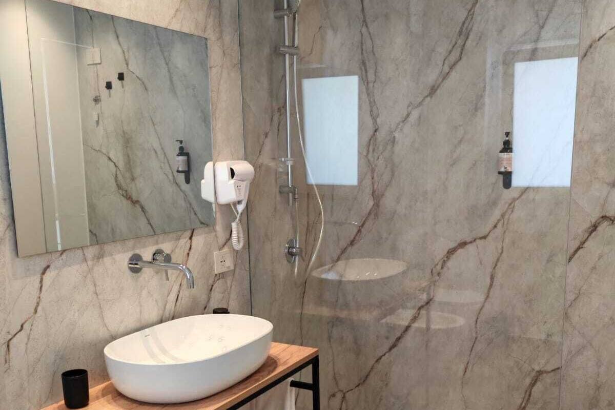 A modern bathroom with a marble wall, a large oval sink, a handheld showerhead, and a mirror.