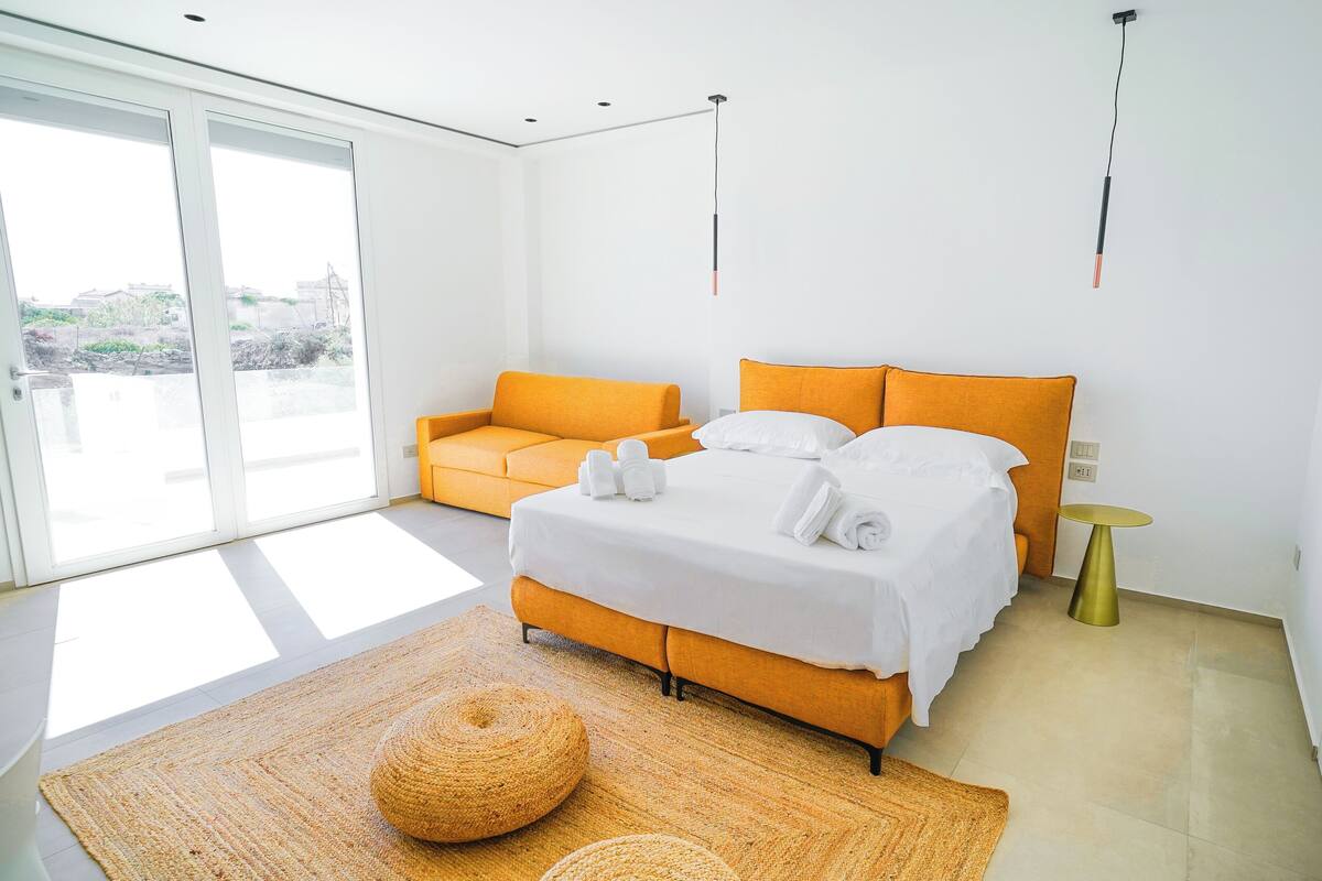 A modern hotel room with a large bed, orange sofa, and a small round table.