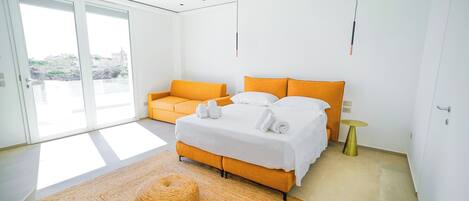 Ein modernes Hotelzimmer mit einem großen Bett, einem orangenen Sofa und einem kleinen runden Tisch.