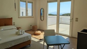 A hotel room with a bed, a small table, a chair, a balcony with a view, and a mirror on the wall. - Dimora Cala Graziosa (Favignana)
