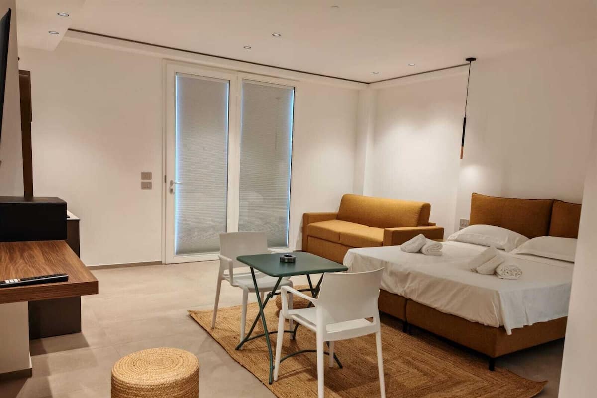 A modern hotel room with a sofa, a bed, a small table, and a TV.