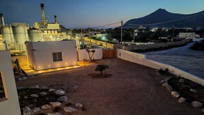 A rooftop garden with a small tree, rocks, and a view of an industrial area and a mountain in the background. - Dimora Cala Graziosa (Favignana)