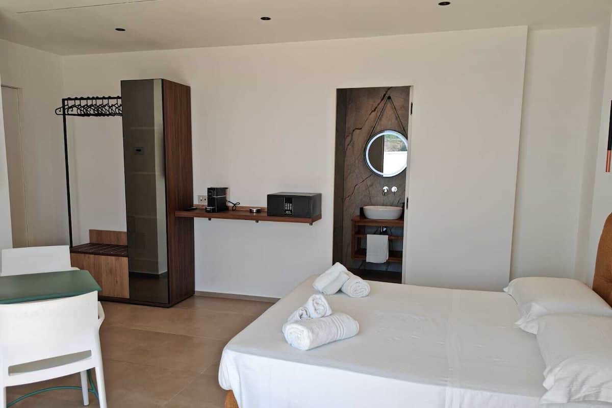 A modern hotel room with a large bed, a desk with a computer, a chair, and a wardrobe.