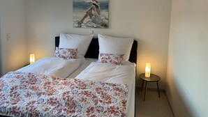 Een slaapkamer met een bed, twee bedlampen, een schilderij aan de muur en een bijzondere plafondlamp.