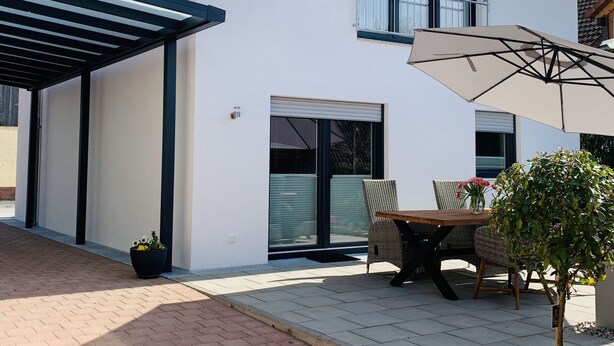 Een modern huis met een overdekte patio, een tafel met stoelen en een potplant.