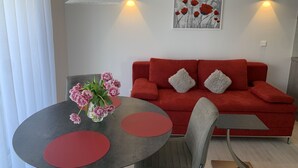 Een moderne woonkamer met een rode bank, een grijze stoel, een ronde tafel met rode details, een bloemenvaas en wandlampen.