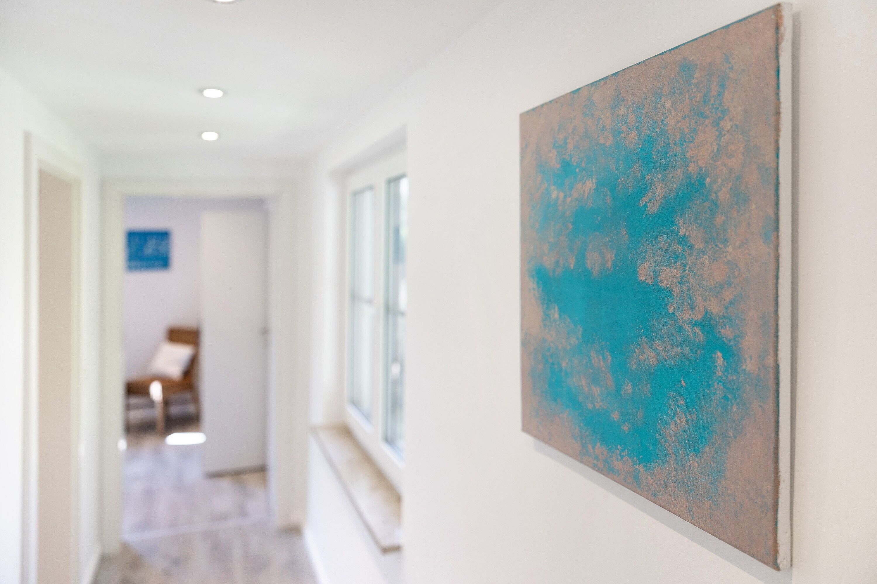 A hallway with a painting on the wall, a window, and a door leading to a room.