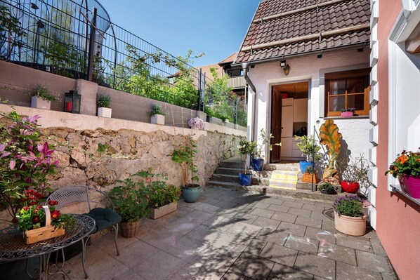 A courtyard with a stone wall, potted plants, a metal table with chairs, and a building entrance. - Holiday Home 'Ludava' with Wi-Fi (Diessen)