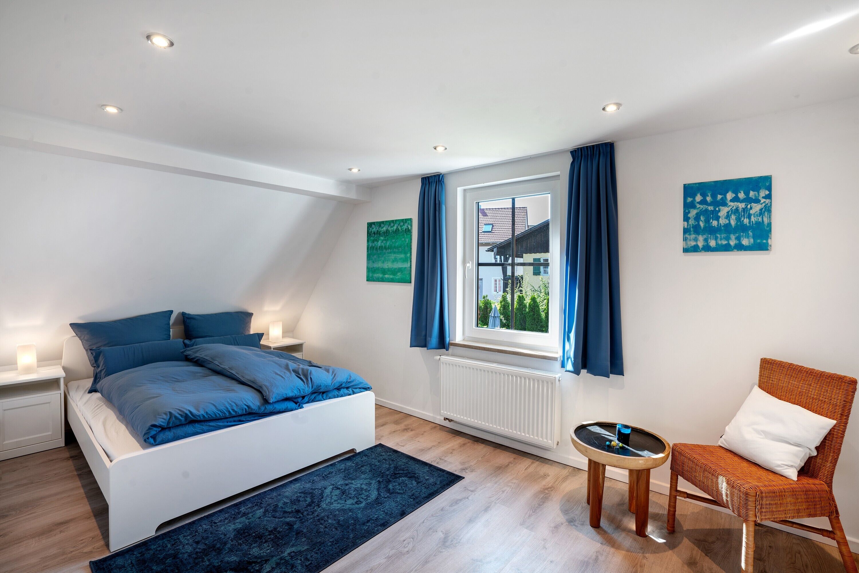 Ein Schlafzimmer mit einem Bett, einem Sessel, einem kleinen Tisch und einem Fenster mit Vorhängen.