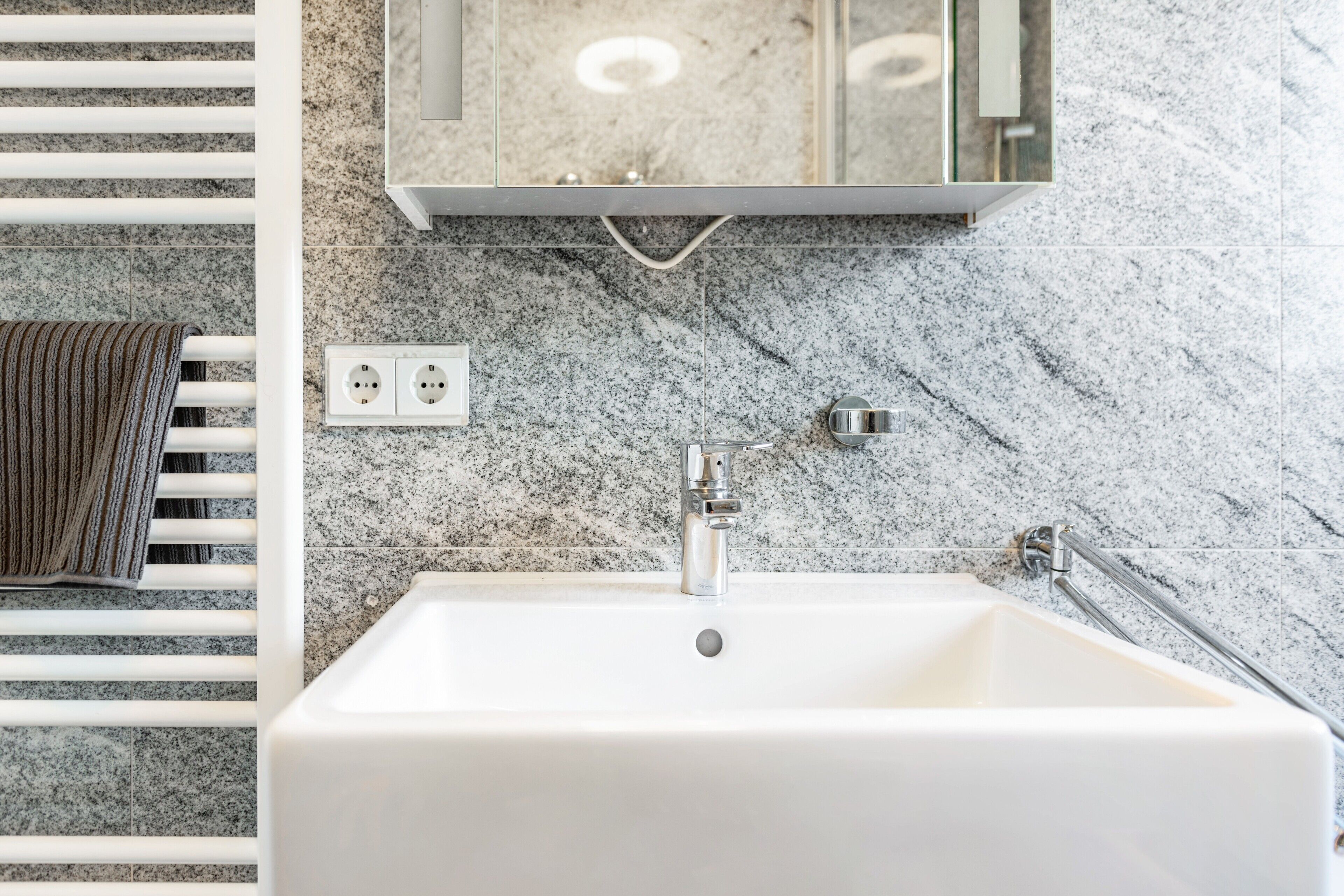 Une salle de bain avec un lavabo blanc, un porte-serviettes, un miroir et un pare-feu en marbre.