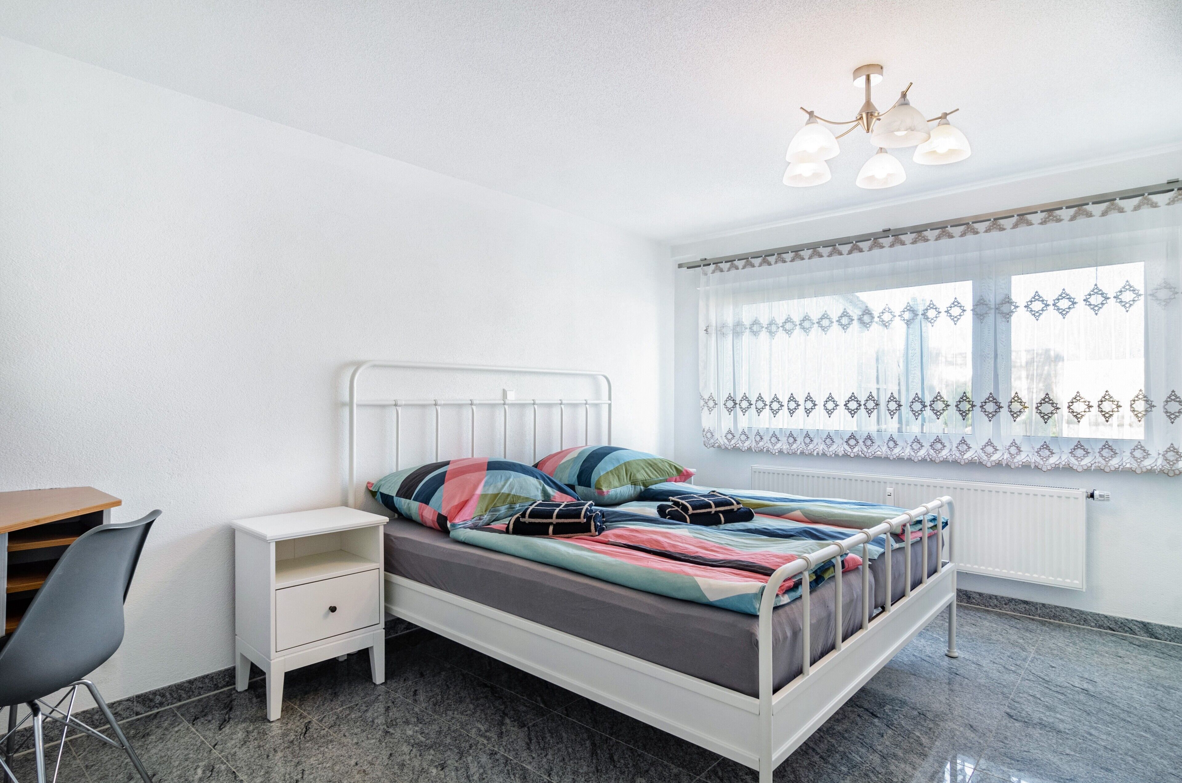 Ein Schlafzimmer mit Bett, Nachttisch, Stuhl und einem Fenster mit Vorhängen.