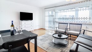 A modern living room with a flat-screen TV, a dining table with chairs, a sofa, and a coffee table.