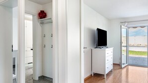 A modern room with a television on a white dresser, a red vase on a shelf, and a view through a glass door.