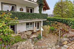 Une maison à l’extérieur blanc, avec un porche abrité comprenant une table et des chaises, et un chemin de pierre menant à l’entrée.