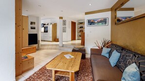A modern living room with a wooden coffee table, a brown sofa with blue cushions, a television, and a kitchen area in the background. - Apartment 'Würtenberger 68 Qm' with Private Terrace, Private Garden and Wi-Fi (Öhningen)