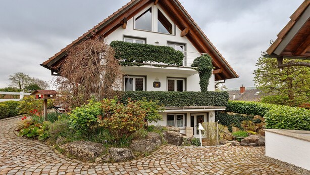 A two-story house with a sloped roof, a balcony with greenery, and a cobblestone driveway. - Apartment 'Würtenberger 68 Qm' with Private Terrace, Private Garden and Wi-Fi (Öhningen)