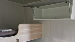 Un lit superposé avec une tête de lit en bois, un bureau escamotable et une petite étagère au-dessus du lit.